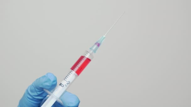 As mãos femininas em luvas médicas azuis com seringa com agulha estão testando a vacina, coletando anticorpos da amostra. Diagnóstico médico para teste de coronavírus ou cura da gripe pelo cientista microbiológico — Vídeo de Stock