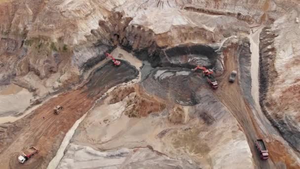 Vista superior de volquetes y camiones de maquinaria son obras en la cantera de arcilla, excavadoras están cargando minerales en camión volquete. Extracción industrial de mineral de hierro. Industria extractiva de canteras. — Vídeo de stock