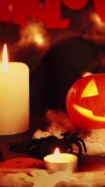 İçi oyulmuş balkabağıyla parlayan ürkütücü bir yüz. Cadılar Bayramı arkaplanı yanan mumlar, örümcekler ve turuncu balkabağı. Cadılar Bayramı selamları. Dikey video