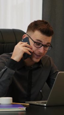 Modern ofiste oturan bir adam telefonla arıyor. Dizüstü bilgisayarın önünde telefonla konuşan gülümseyen bir erkek. Dikey video