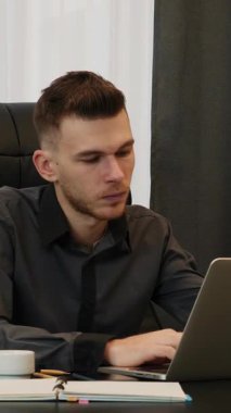 İş adamı laptop ekranına bakıyor ve gözlüğünü çıkarıyor, yoğun bir iş gününden sonra yorgun. Erkek, kafasına elleriyle dokunur ve iş yerinde otururken gözlüğünü çıkarır. Dikey video