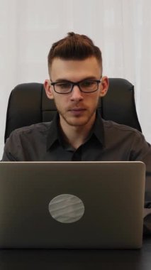 Gözlüklü adam evden dizüstü bilgisayarla çalışıyor. Ofiste oturan bir erkek dizüstü bilgisayar projesinde çalışıyor. Dikey video