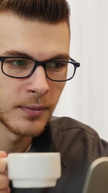 Modern ofiste oturup kahve içen bir adamın portresi. Kahve içip dizüstü bilgisayar ekranına bakan işadamlarına yakın çekim yapın. Dikey