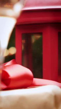 Kırmızı kurdeleli el işi kağıdına sarılmış hediye, şampanya ve Noel süslemeleri dönüyor, kapat. Noel ve yeni yıl dekorasyonlarıyla dolu bir arka plan. Dikey video