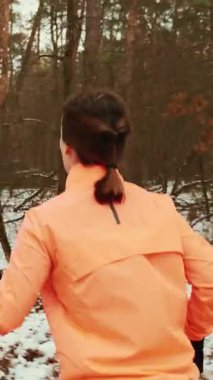 Kış parkında koşan aktif bir kadın. Genç ve çekici bayan sporcunun sabahları spor kıyafetleri içinde koşuşunun arka görüntüsü. Dikey video