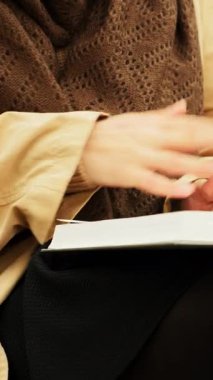 Kadın elleri kitabı açıp sayfaları çeviriyor. Kitap okuma konsepti. Güz parkında kitap okuyan kahverengi eşarplı bir kadın. Dikey video