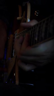 Karanlık odada, erkek ellerinin yakın çekimi elektro gitarla ve ışıklarla yapılıyor. Erkek müzisyen gitar penası kullanarak gitar telleriyle çalar. Dikey video