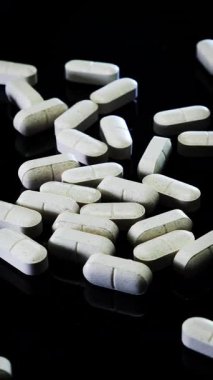 Haplar ve uyuşturucular siyah arka planda dönüyor. Masadaki beyaz haplar, kapatın. Eczacılık işi. Dikey video