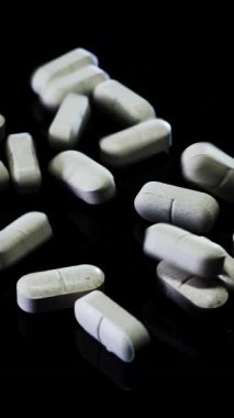 Siyah arka plana beyaz haplar dökülüyor. Tabletler masaya düşüyor ve dönüyor. Tıp konsepti. Dikey video