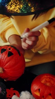 Cadılar Bayramı, dekorasyon ve tatil konsepti. Turuncu balkabağına korkunç bir yüz çizen kadın mı yoksa Cadılar Bayramı için dekore edilmiş odada balkabağı feneri mi? Dikey video