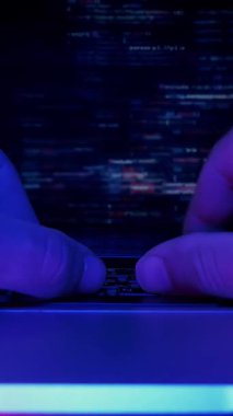 Kişi karanlık bir ofiste dizüstü bilgisayarın önünde çalışıyor, programlama kodu yazıyor, elleri kapatıp ekranı gösteriyor. Eller bilgisayar klavyesinde yazıyor, kod ekranda gösteriliyor. Dikey video