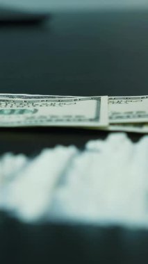 Kokain tozunu kara masaya yakın tut ve adam bize arka planda dolar sayıyor. Dolar banknotlarının yanında kokain ya da beyaz uyuşturucu tozu. Dikey video