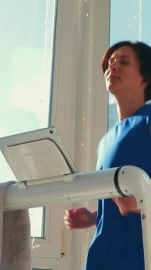 Koşu bandında çalışan gülümseyen genç bir kadın. Spor giyim bölümünde koşu bandında koşan bir kadın. Evde fitness eğitimi. Dikey video