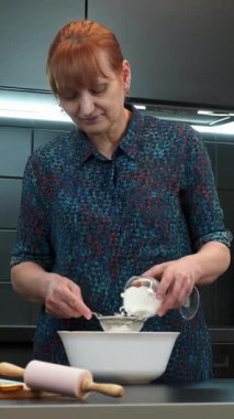 Olgun kadın evde kek pişiriyor, klozete un ekliyor. Modern mutfakta tatlı hazırlayan kadın. Evde fırın var. Ev yapımı pişirme. Dikey video