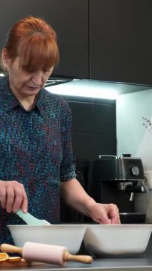 Kadın spatulaya malzeme ekleyip karıştırıyor, ev yapımı kek hazırlıyor. Kadın evde tatlı hamur işi pişiriyor. Dikey video