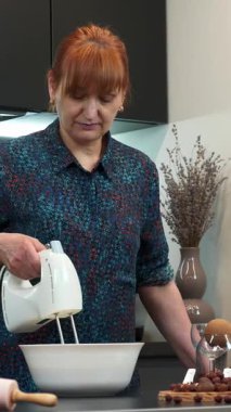 Elinde elektrikli mikser tutan ve modern mutfakta hamuru kaseye karıştıran kadın portresi. Kadın fırıncı ev yapımı tatlı kek hazırlıyor. Dikey video