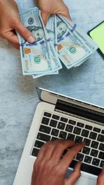 Dizüstü bilgisayarda daktilo kullanan bir adam ve nakit para sayan bir kadın, yakın çekim. İş konsepti. Dikey video