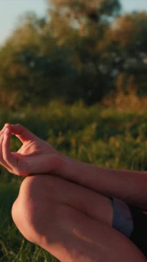 Gün doğumunda meditasyon yapan genç bir adamın portresi. Erkek nilüfer pozisyonunda sabahları yoga yapıyor, temiz havanın ve doğanın tadını çıkarıyor. Gün batımında yoga. Dikey video