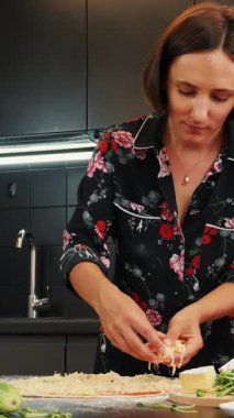 Pizzaya peynir ekleyen kadın İtalyan pizzası margherita hazırlıyor. Kadın evde lezzetli pizza yapıyor, pizzaya peynir ekliyor. Dikey video