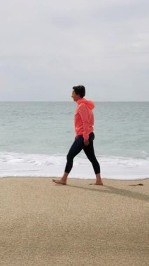 Gülümseyen mutlu kadın fırtınalı bir günde tropikal sahilde yürüyor, özgürlüğü ve mutluluğu hissediyor. Tasasız genç kadın okyanus boyunca yürüyor, güzel denizin tadını çıkarıyor. Dikey video