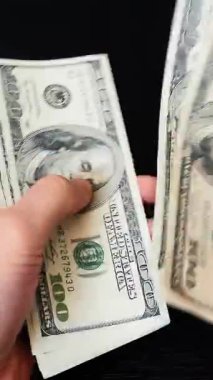 Erkek elinde bir tomar para tutuyor ve para sayıyor. Dikey video. Bir kişi yüz Amerikan doları banknotları sayar. Finans ve iş konsepti