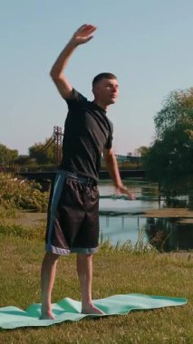 Adam parkta yoga egzersizi yapıyor. Yoga minderinin üzerinde uzanan güçlü genç bir erkek. Yoga hareketleri ve sabah çim üzerinde pozisyon pratiği yapan biri. Güçlü bir atlet. Dikey video