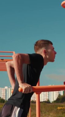 Atletik adam şehir parkındaki yatay bara daldı. Spor aktiviteleri açık alanda. Kollar için spor ve güç egzersizleri. Dikey video