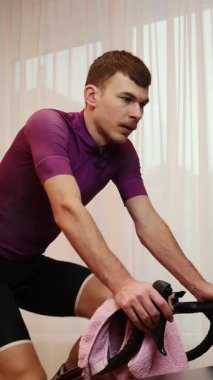 Bisikletçi eğitiminde akıllı bisiklet eğitmeni ve yüzünü havluyla siliyor. Egzersiz bisikletinde kardiyo fitness yapan bir adam. Dikey video