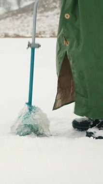 Gölde buz kuyusu kazan balıkçıları kapatın. Balıkçı kış balıkçılığında donmuş gölette buz deliği açıyor. Dikey video