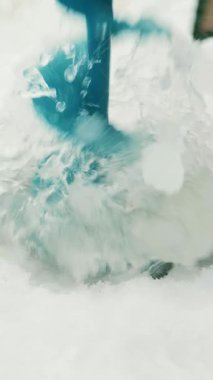 Buz matkabı donmuş nehirde buz deliği açıyor, yaklaşın. Balıkçı, buz matkabıyla buz deliği açıyor. Kış balıkçılığı. Dikey video