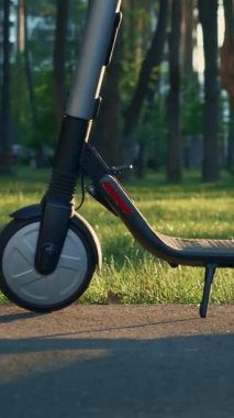 Şehir parkında elektrikli scooter kullanan takım elbiseli kadın bacakları ve spor ayakkabıları. İş elbiseli bir kadın elektrikli scooter kullanıyor. Dikey video