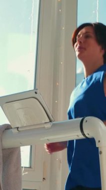 Formda genç bir kadın evde koşu bandında koşuyor. Atletik güdümlü kadın kilo vermek için koşu bandında koşuyor. Dikey video