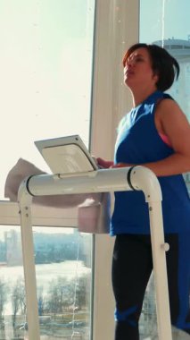 Motive olmuş sportif kadın koşu bandındaki yoğun fitness egzersizleri sırasında yüzünü havluyla siliyor. Evde kardiyo çalışması. Dikey video