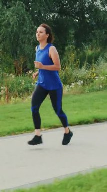 Sabahları gezinti güvertesinde koşan bir kadın. Parkta spor yapan bir kadın kardiyo egzersizi yapıyor. Sokakta koşan aktif bir kadın. Dikey video