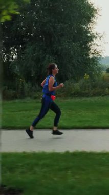 Sabahları spor elbiseli bir kadın koşuyor. Atletik genç bayan rıhtımda sakin nehir boyunca koşuyor. Sabah egzersizleri. Fitness ve sağlıklı yaşam konsepti. Dikey video