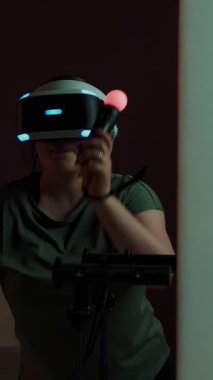 Genç bir kadın interaktif oyun oynuyor VR gözlük takıyor, joystick kullanıyor. VR gözlüklü kız oturma odasında video oyunu oynuyor. Dikey video