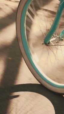 Eski model bisikletin dönen çarkını kapat. Yazlık elbiseli ve beyaz spor ayakkabılı bir kız gün batımında bisiklet sürüyor, bisiklet takımlarını ve bacaklarını kapatıyor. Dikey video