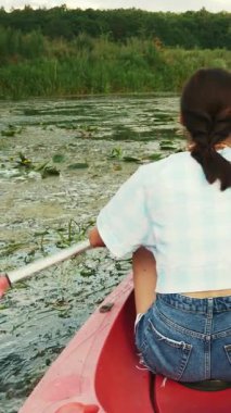 Kız kanoyla nehri keşfediyor. Kadın yazın kanoya biniyor. Dişi, nehirde kanoda yüzüyor. Dikey video