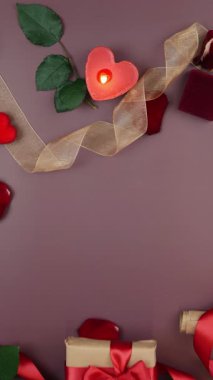 Eller, Sevgililer Günü için paketlenmiş kırmızı kurdeleli hediye paketi. Kadın 14 Şubat 'ta hediyesini hazırlıyor. Masada güller ve yanan mumlarla. Dikey video