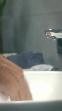Kadın ellerini havluyla yıkıyor ve kurutuyor. Kadın ellerini lavaboda köpükle yıkıyor, su ellerden akıyor. Dikey video