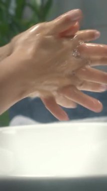 Kadın ellerini sabun ve sıcak suyla yıkıyor, parmaklarını sıkça ovuyor. Pandemik önleme. Kadın lavaboda köpükle ellerini yıkar. Dikey video