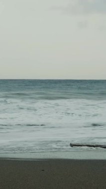 Deniz dalgaları ve kumlu plajları olan güzel bir sahil şeridi. Büyük dalgalar sahile vurur, su sıçratır ve beyaz köpük oluşturur. Dikey video