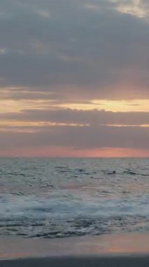 İnanılmaz deniz batımı. Fırtınalı denizin üzerinde gün batımı, su yüzeyine yansıyan turuncu ışık. Güzel sahil şeridi ve gün batımında deniz kıyısında. Dikey video