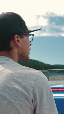 Man driving electric boat ship, turning wheel, back view. Male sailing on tourist ship along mountain lake. Vertical video