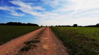 Yeşil çayırlar boyunca toprak çakıl yolunda araba sürüyorum. Kırsal kesimde, POV. Güneşli yaz gününde kırsal alanda bisiklet süren kişi, bisikletçi bakış açısı.