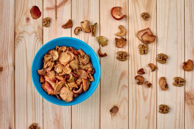 Sağlıklı gıda: kurutulmuş elma bir plaka üzerinde. Ahşap yüzey ile dağınık fındık ve kuru elma. Üstten görünüm.