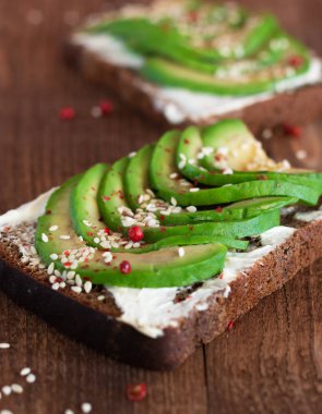 ahşap masa üzerinde avokado dilimleri ile krem peynir ekmeği