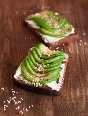 ahşap masa üzerinde avokado dilimleri ile krem peynir ekmeği