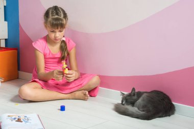 A girl is making figures out of colored paper, a domestic cat is sleeping nearby clipart