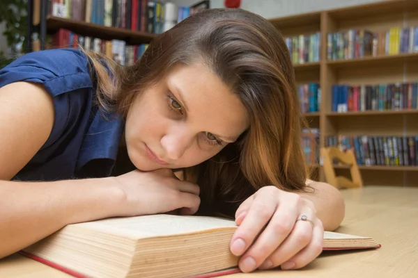 累了的女孩在图书馆的桌子边看书 — 图库照片